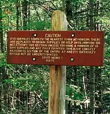 Wooden sign reading "Caution. It is 100 miles south to the nearest town at Monson. There are no places to obtain supplies or help until Monson. Do not attempt this section unless you have a minimum of 10 days supplies and are fully equipped. This is the longest wilderness section of the entire AT and its difficulty should not be underestimated. Good hiking! MATC"