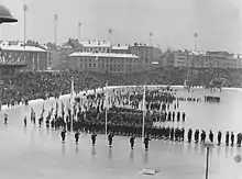 Long-shot of Olympic stadium with many athletes standing in neat formation behind their national flags