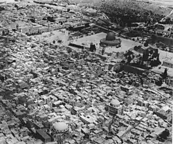 Aerial view of city in front of a plaza with a domed building, with a terraced hill behind