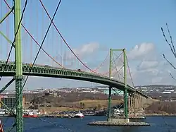 A metal suspension bridge painted green, with orange cables.