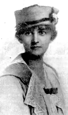 A young white woman wearing a light colored pillbox hat and a coat with a lace collar visible