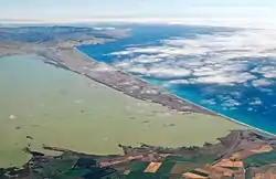 Aerial photo showing long triangular spit with green lakewater to the left and the ocean to the right