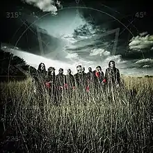 A group of nine men wearing masks stand in a field of grass with a gloomy clouded sky above them.