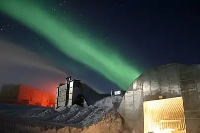 A photo of the station at night. The new station can be seen in the far left, the electric power plant is in the center, and the old vehicle mechanic's garage in the lower right. The green light in the sky is part of the aurora australis.