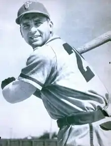 A man in a white baseball uniform and a dark cap holds his bat, ready to swing