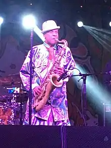 Angelo Moore in a white bowler hat playing a saxophone