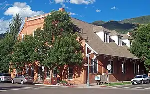 A brick building with trapezoidal roof overhanging the sidewalk on its right side at an intersection. Signs say it is at the 100 block of South Galena Street and the 500 block of East Hopkins Avenue.