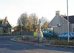 A war memorial along a street with houses and cars