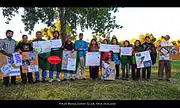 Bangladeshis of all ages holding signs in front of a tree