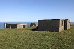 A collection of concrete buildings in a field with the sea beyond