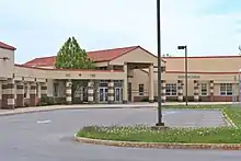 Photograph of a sandstone colored brick school building with a tall atrium and red, corrugated steel roof