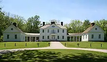 A white Palladian mansion, flanked by a wing on either side, and fronted by a green lawn in the foreground