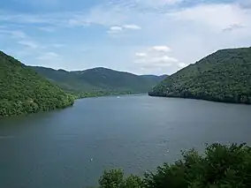 A reservoir flanked by a green forested mountain ridge on either side.