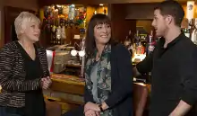 Three people standing in a pub; an older woman on the left, a younger women in the middle, and a man on the right