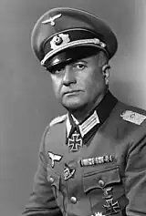 A man wearing a military uniform, peaked cap and neck order in the shape of a cross.