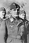 A man wearing a military uniform, side cap, various military decorations including an Iron Cross displayed at the front of his uniform collar.