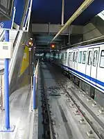 An underground station with two tracks in Madrid. A blue and white subway train is entering the station on the left.