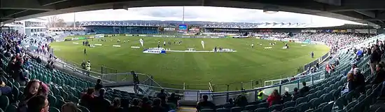 View of a grassed sporting field and a variety of small stands. Some people on field and in the stands.