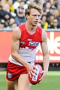 Male athlete in sleeveless guernsey prepares to kick football