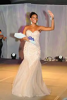 chocolate-skinned lady on a white long dress waving while holding a bouquet