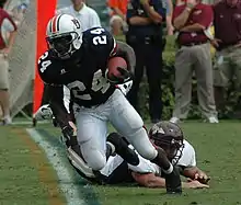 An American football player is in position on the field. He is wearing a red jersey with the number 11 across the back and white pants.