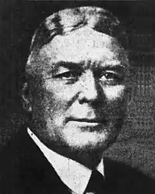 A black-and-white photographic portrait of Harvey from the shoulders up, wearing a suit