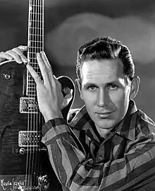 A black-and-white photo of country singer Chet Atkins, holding a guitar upright.