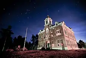 An old, two-story brick courthouse with third-story bell tower under a starry night sky.