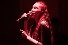 A woman with long hair sings into a microphone under dim red lighting