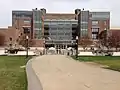 A slightly curved concrete path running through a grass lawn and leading to a street, behind which sits Coffman; its lower level entrance up a small flight of stairs