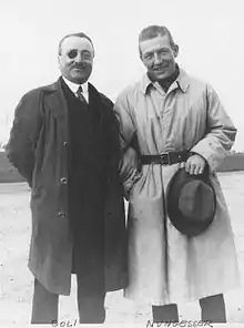 Period photograph shows pilots François Coli and Charles Nungesser in informal clothing; Coli on the left is in street clothes while Nugesser is in a long flight jacket.