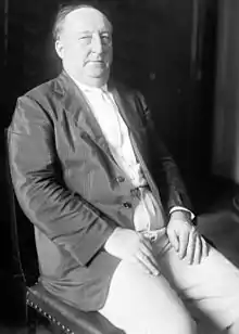 Upper body and head of seated middle-age man wearing sport coat with white shirt and tie