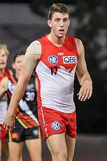 A light-skinned man with black hair standing in a red and white guernsey with red shorts