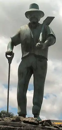 Stone statue of a middle aged-man with a beard, a shovel, and some other similar instrument