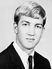 A young man in a suit looks directly at the camera, slightly smiling.