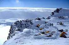 Several tents are pitched near the edge of a snow-covered cliff