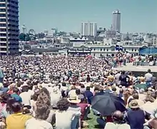 A large crowd. Far away is a platform, and a banner reading SHAME FRASER SHAME.