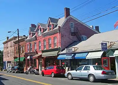 A two-lane highway with an additional lane for street parking is flanked by shops housed in old buildings.