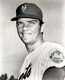 An man in a light baseball jersey and dark cap