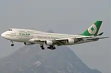 Aircraft in flight. Side view of quad-engine jet with extended landing gear and flaps.