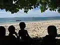 Children on the beach at Tuo village,  Fenualoa with a visiting yacht in the background.