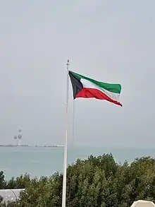 The Flag of Kuwait waving in the Green Island and the Kuwait Towers in the background