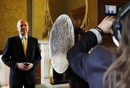 A lighting technician holds a reflector to diffuse the light falling on a politician