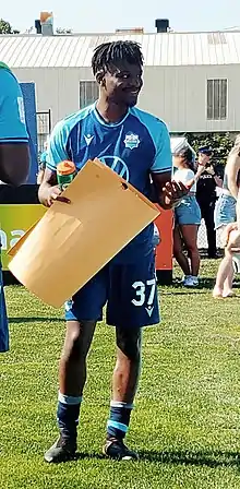 Lifumpa Mwandwe in uniform holding a folder paper sign