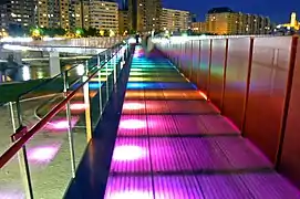 Bridge at night with multicoloured LED lights lighting the bridge from below; each successive panel is lit in a different colour.