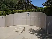 A paneled, marble wall decorated with a seal and some inscribed words. A plaque with name and dates rests on the shiny marble floor.