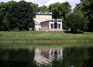 Photograph of 18th century buildings in a park with trees, grass, and a lake