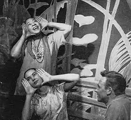  A crouching man in military uniform watches a young woman and a middle-aged one make hand gestures to him