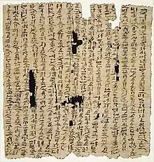 A museum display of an ancient fragment of a papyrus document safeguarded by sealed thick glass, with cursive hieratic handwriting in black ink on its surface