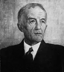 A black and white portrait of an older gentleman  with a receding hairline wearing a suit and tie.